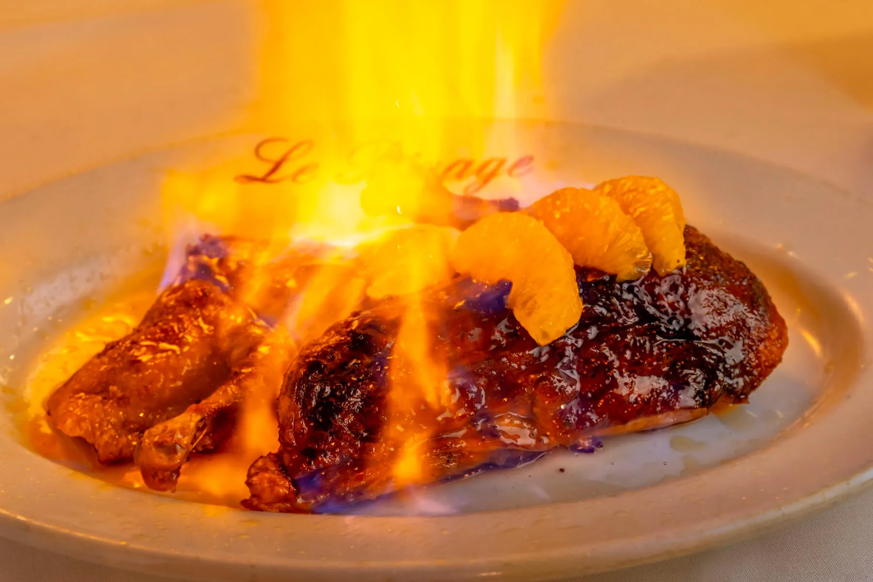 Flaming dessert with caramelized orange segments on a white plate.